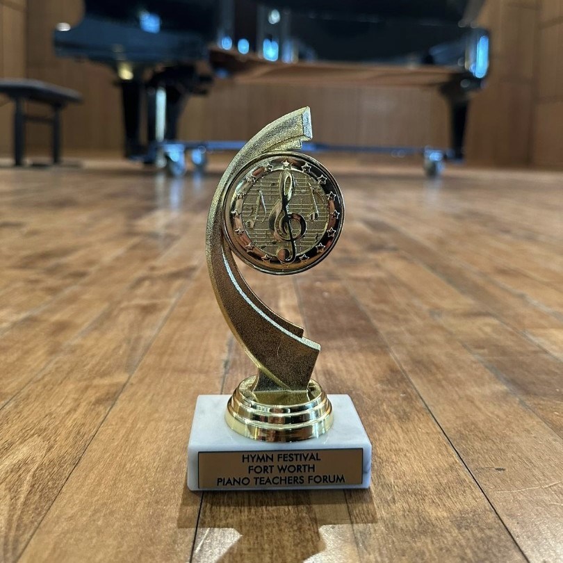An image of a trophy prominently displayed on a stage in front of a grand piano, symbolizing excellence and achievement in the world of piano performance.