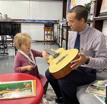 Image of a teacher and her student participating in the Music for Toddlers program in Benbrook. The teacher is showing a guitar to the young student, creating a playful and engaging musical learning environment.