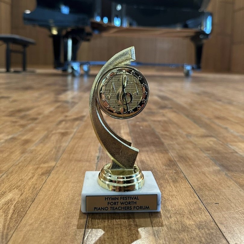 An image of a trophy prominently displayed on a stage in front of a grand piano, symbolizing excellence and achievement in the world of piano performance.