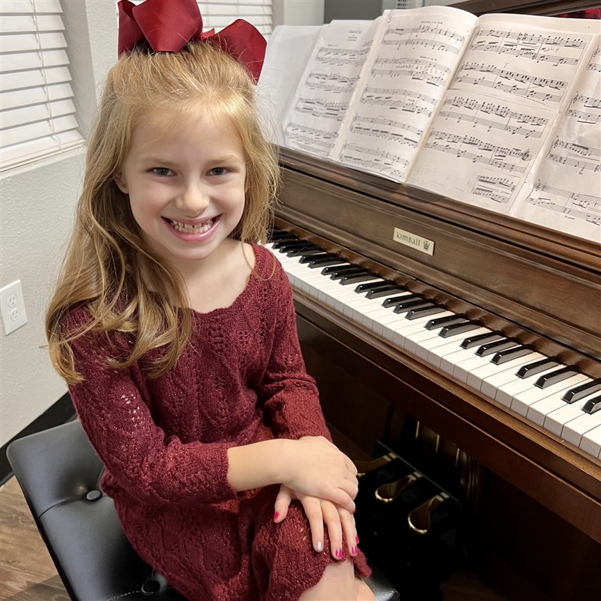 Image of a student sitting contentedly beside a piano following a recital in Fort Worth, reflecting on their performance and musical journey.